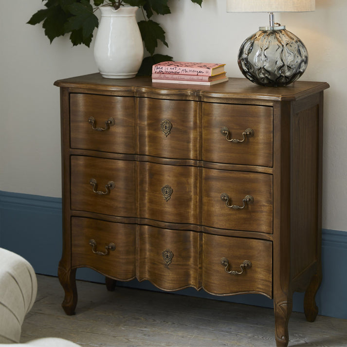 The Esla Walnut 3 Drawer Chest adds elegance to any space, whether upstairs or downstairs. A charming chest made of solid and veneered panels, in an aged walnut finish. It boasts traditional design elements such as cabriole legs and graceful curves, reminiscent of classic French styling. With three generously-sized drawers, this piece offers abundant storage space, enhanced by antique brass fittings.